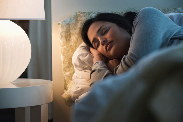 Lamp illuminating sleeping Hispanic woman Beeld Getty Images